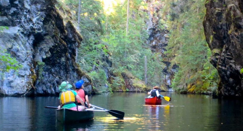 outward bound students paddle two canoes on still water surrounded by greenery